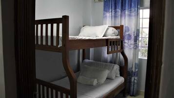 A bunk bed with a lower bunk, a window with blue curtains, and a view of greenery outside.