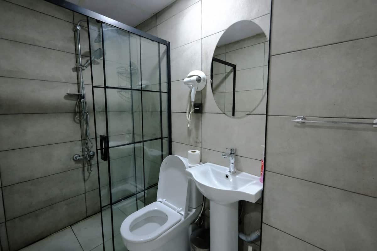 Un baño con cabina de ducha de vidrio, inodoro blanco, lavabo con espejo y paredes de azulejos.