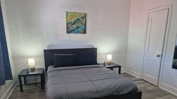 A bedroom with a bed, two bedside tables, a nightstand, a door, and a wall with a painting. - Nice renovated 1 bedroom Apartment Sunny Days Motel 3 (St. Petersburg)