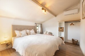 A bedroom with a large bed, bedside lamps, a ceiling light fixture, a window with curtains, and a built-in shelving unit. - Novapark V41 - modern fisherman's cottage with large enclosed terrace (De Haan)