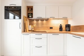 A modern kitchen with white cabinets, a wooden countertop, a built-in oven, and a coffee maker. - Novapark V41 - modern fisherman's cottage with large enclosed terrace (De Haan)