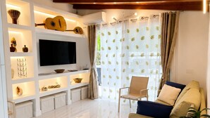 Un salon moderne avec un téléviseur à écran plat, des étagères ornées d’objets décoratifs, un canapé et un fauteuil.