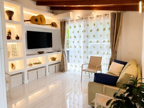 A modern living room with a flat-screen TV, shelves with decorative items, a sofa, and a chair. - Mimosetta Guest House: A Cozy Cottage Surrounded by Peace and Greenery, with Views of the Sea and Mountains (Vallebona)