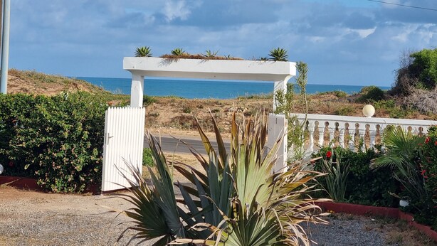 Ein Küsteneigentum mit einer weißen Pergola, einem Kiesweg und Blick auf das Meer.
