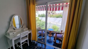 Ein Zimmer mit Schreibtisch, Spiegel, Stuhl und Blick durch eine Glastür auf einen Außenbereich mit Tisch und Stühlen.