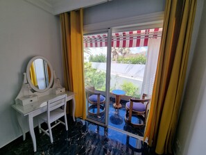 A room with a desk, a mirror, a chair, and a view through a glass door to an outdoor area with a table and chairs. - 1 bedroom seaside apartment (El Jadida)