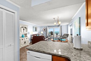 Eine Küche mit Granit Arbeitsplatte, Geschirrspüler, Essbereich mit Tisch und Stühlen, Blick auf den Ozean und ein Wohnzimmer mit Sofa und Kamin.