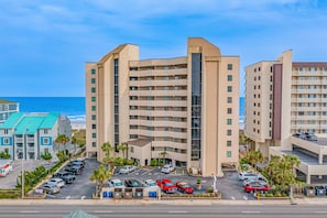 Ein mehrstöckiges Hotel mit Parkplatz, Meerblick und moderner Architektur.