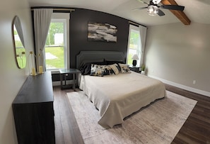 Ein Schlafzimmer mit Bett, Kommode, Spiegel, Deckenventilator und Fenster.