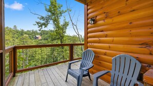 Un pontile in legno con due poltrone Adirondack, una ringhiera e vista su una zona boscosa.