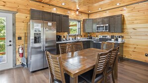 Una cucina con rivestimenti in legno, elettrodomestici in acciaio inossidabile, un tavolo da pranzo con sedie e un estintore.