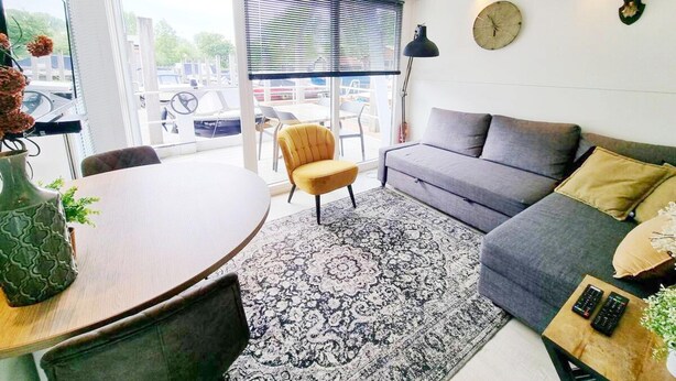 Un salon moderne avec un canapé, une table ronde, un fauteuil jaune, un tapis à motifs et une horloge au mur.