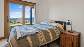 A bedroom with a bed, a nightstand, and a view of the outdoors. - Lodges 12 | Lake Views | Modern Condo (Rangeley)