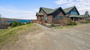 A wooden house with a green roof, a gravel driveway, and a view of a lake. - Lodges 12 | Lake Views | Modern Condo (Rangeley)