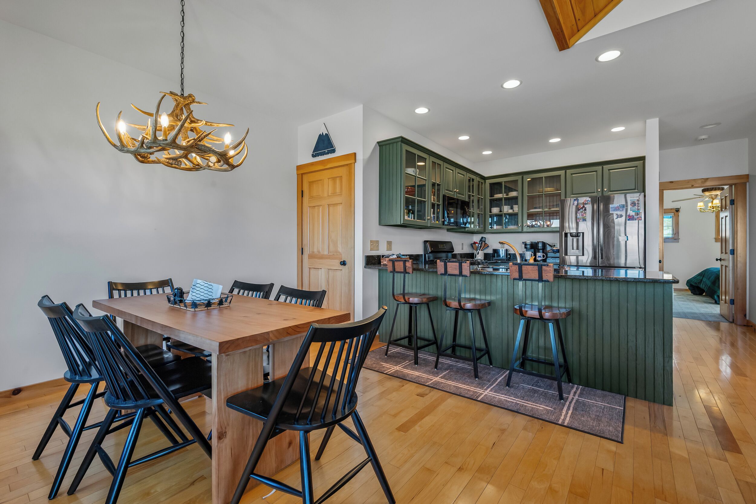 A modern kitchen with green cabinets, a wooden dining table, and bar stools.