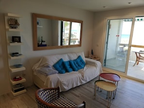A living room with a sofa, a chair, a table, a bookshelf, a mirror, and a sliding glass door leading to an outdoor area. - Deltamar 81, Solo Familias! (Playa Xeraco)