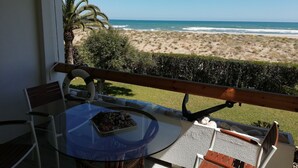 Un balcon avec une table en verre, des chaises et une vue sur la plage et l’océan.