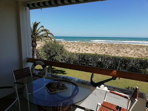 A balcony with a glass table, chairs, and a view of the beach and ocean. - Deltamar 81, Solo Familias! (Playa Xeraco)