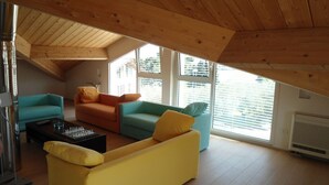A loft-style living room with a sloped ceiling, wooden beams, and large windows. - Villa Celeste Flexrent - Abissinia Real Estate (Scacciano)