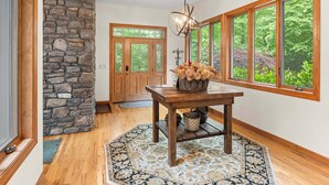 A room with a stone wall, wooden door, and windows with a view of greenery. - 3BR, 3BA Mountain home with sweeping views in Waynesville. (Waynesville)