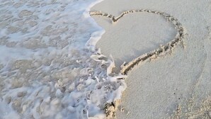 A beach with a heart-shaped sand drawing and a clear view of the ocean.