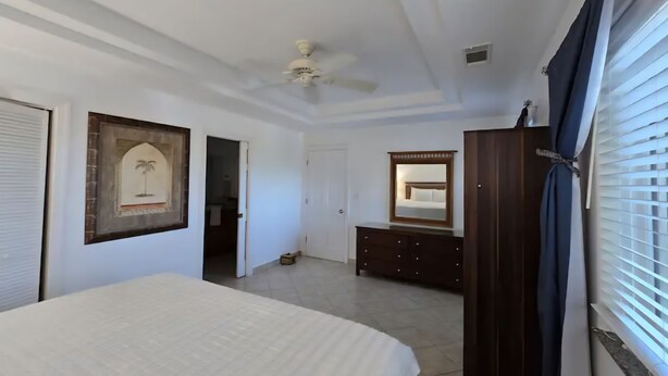 A bedroom with a bed, a ceiling fan, a dresser, a mirror, and a door leading to another room.