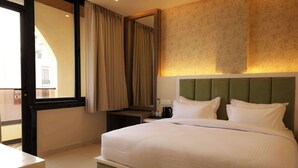 Habitación de hotel con una cama grande, una mesita de noche, una cafetera y vistas a través de una ventana con cortinas.