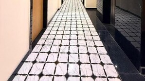 Un pasillo de hotel con suelo de baldosas, puertas, cuadros enmarcados en las paredes y una lámpara en el techo.
