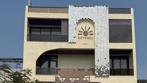 Un edificio con un letrero que dice 'NOVOSOL' y un logo con un sol y una flor. Hay tres coches estacionados en la parte delantera.