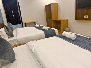 Ett hotellrum med två sängar, en garderob i trä, ett litet bord och en tv som är monterad på väggen.