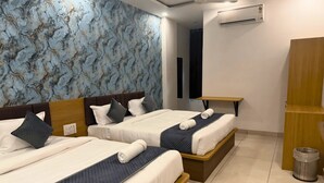 Habitación de hotel con dos camas, cabecero de madera, una mesita, unidad de aire acondicionado y un bote de basura.