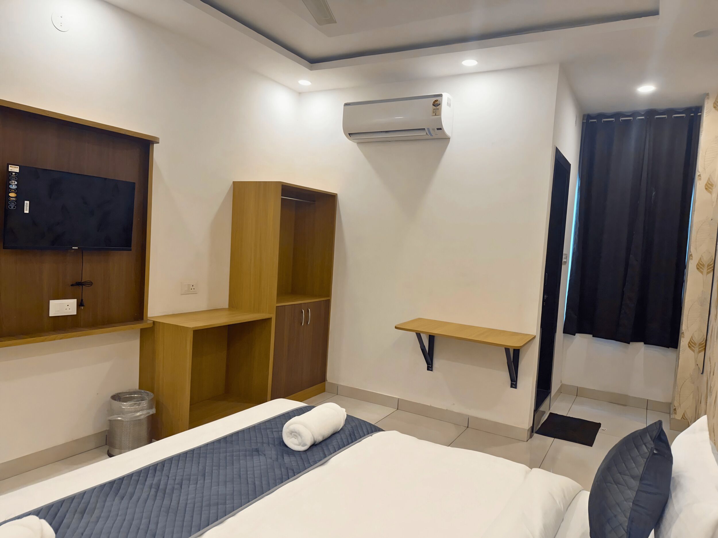 Ein Hotelzimmer mit Bett, Wandfernseher, Kleiderschrank, kleinem Tisch und Klimaanlage.