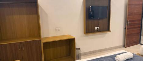 A hotel room with a bed, a wooden wardrobe, a television mounted on the wall, and a door.