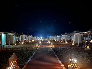 A row of tents with a central walkway, each tent has a canopy and is equipped with outdoor seating.