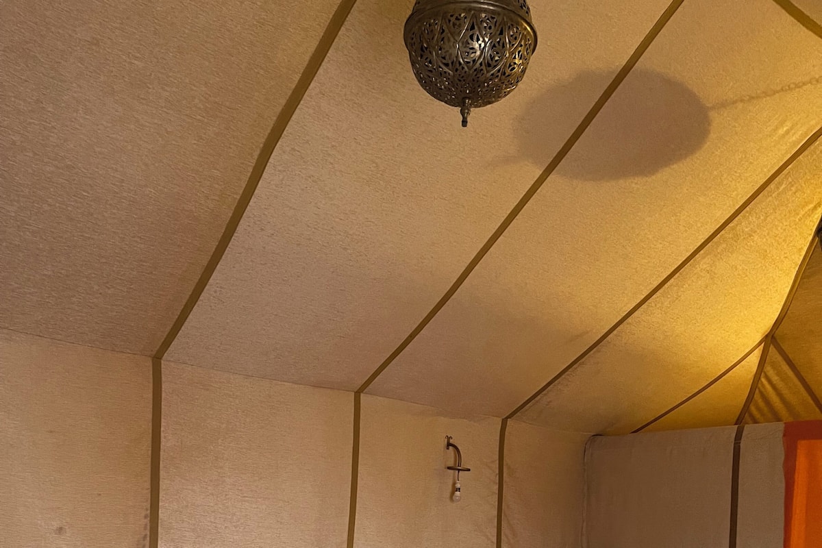 Una cama con cabecera, almohadas, una manta y una lámpara colgante en una habitación con forma de tienda.