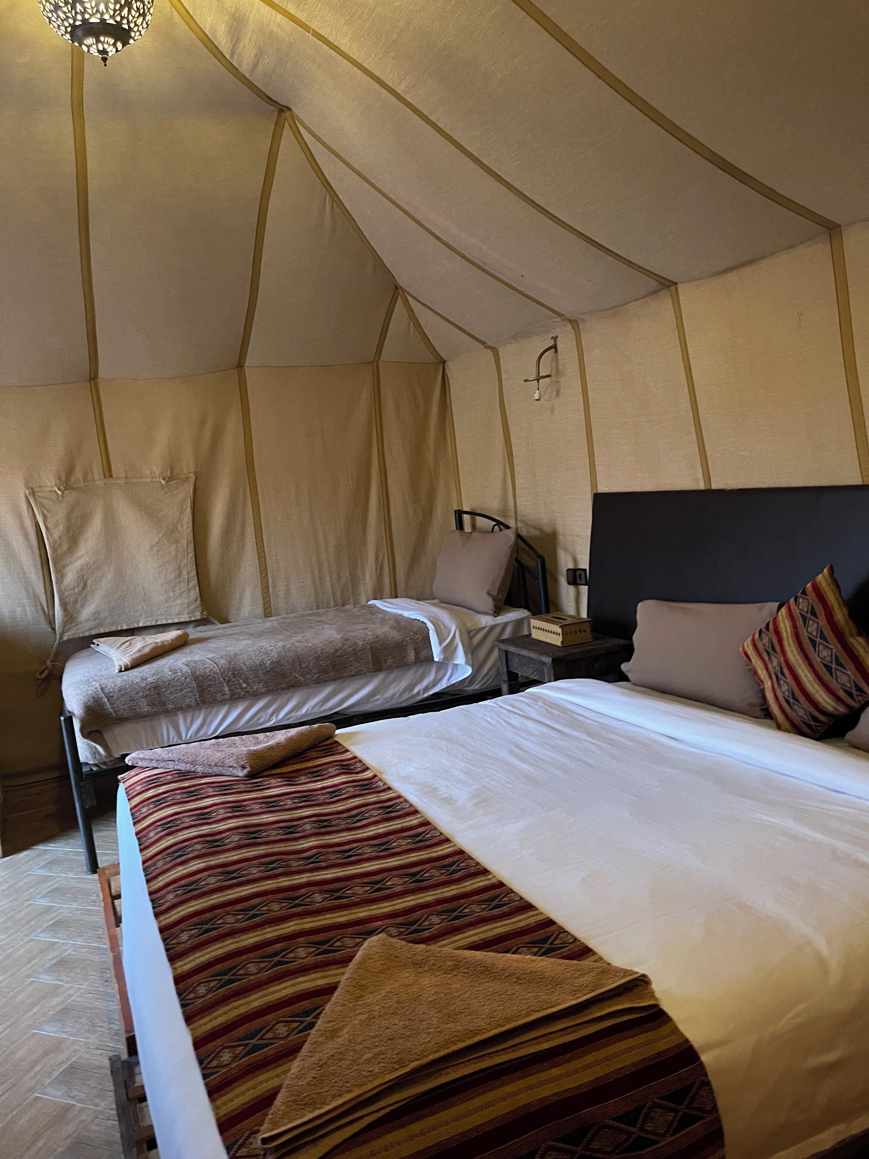 A tent-style room with two beds, a nightstand, and a hanging light fixture.
