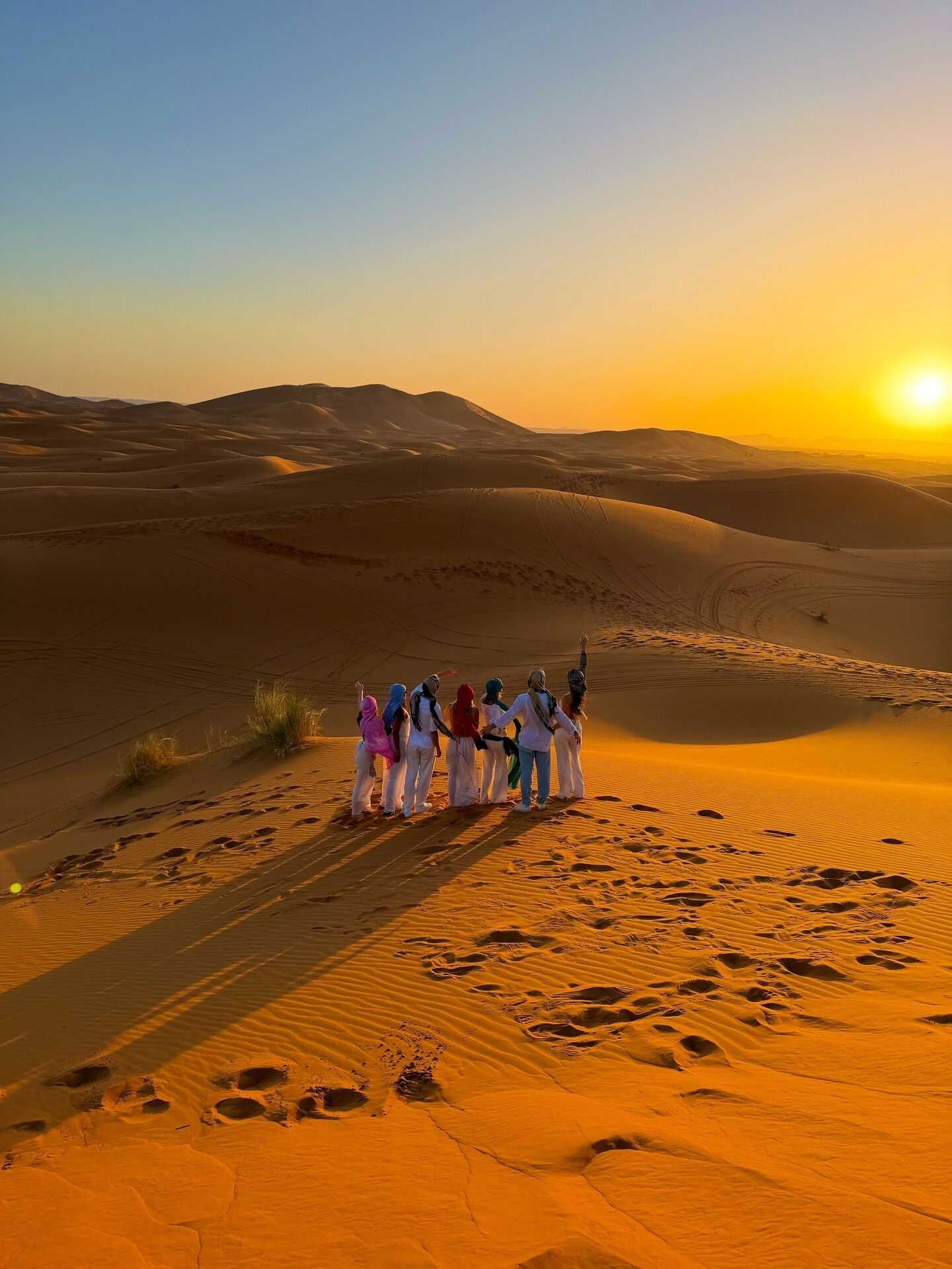 A group of people standing on a sand dune with a sunset in the background.