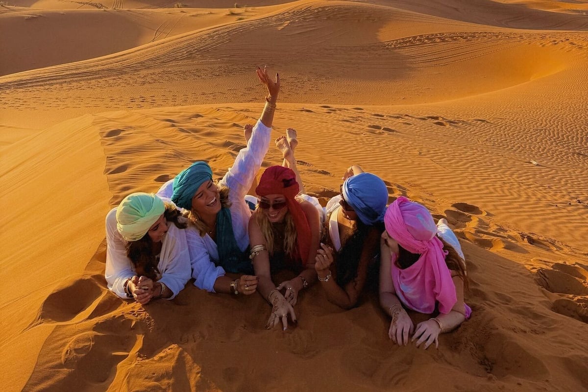 Un grupo de personas sentadas sobre dunas de arena en un paisaje desértico.