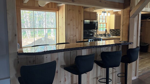 A wooden kitchen with a large window, a black countertop, and three bar stools. - Welcome to "the east Madison chapel" (Madison)