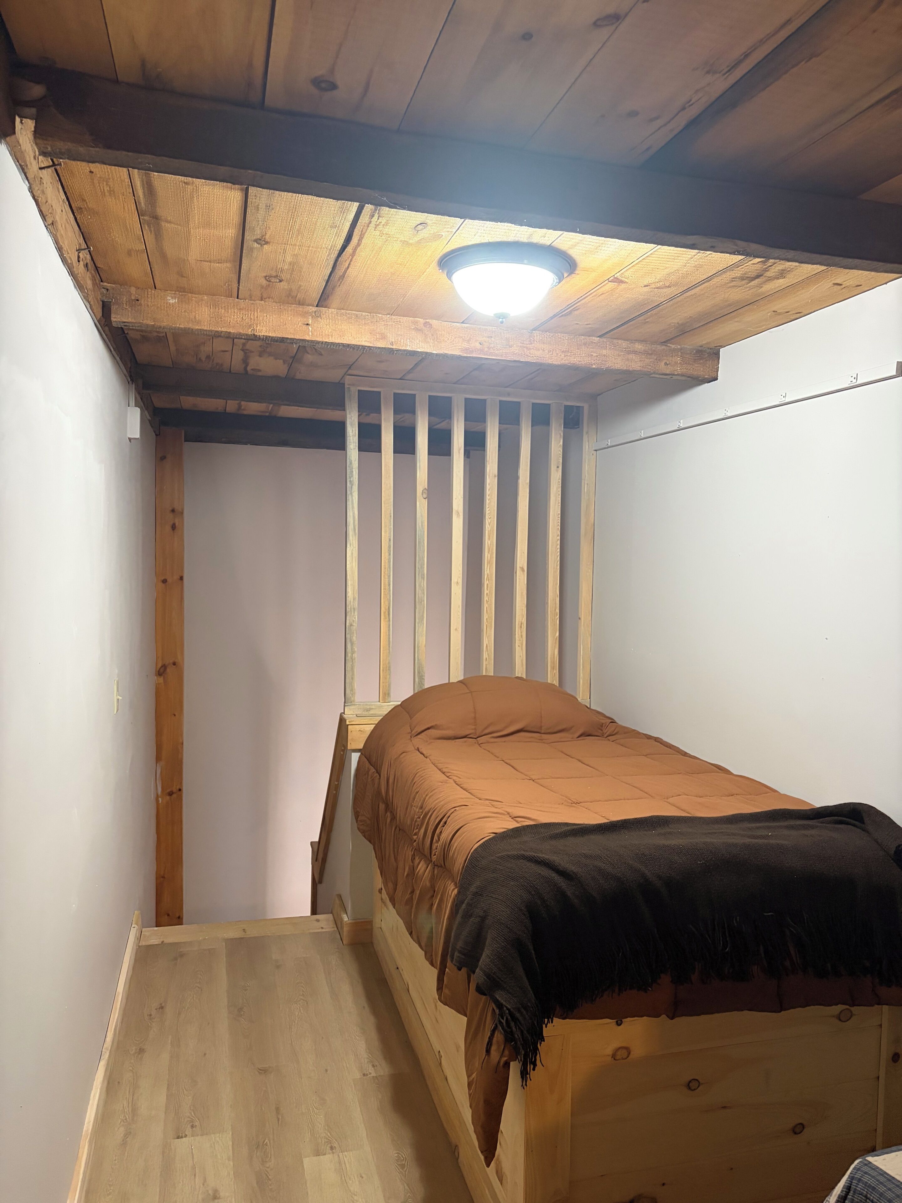 Une petite pièce étroite, avec un lit superposé en bois, un plafond en pente et un seul luminaire.