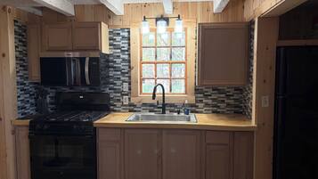 A kitchen with wooden cabinets, a black stove, a microwave, and a window with a view.
