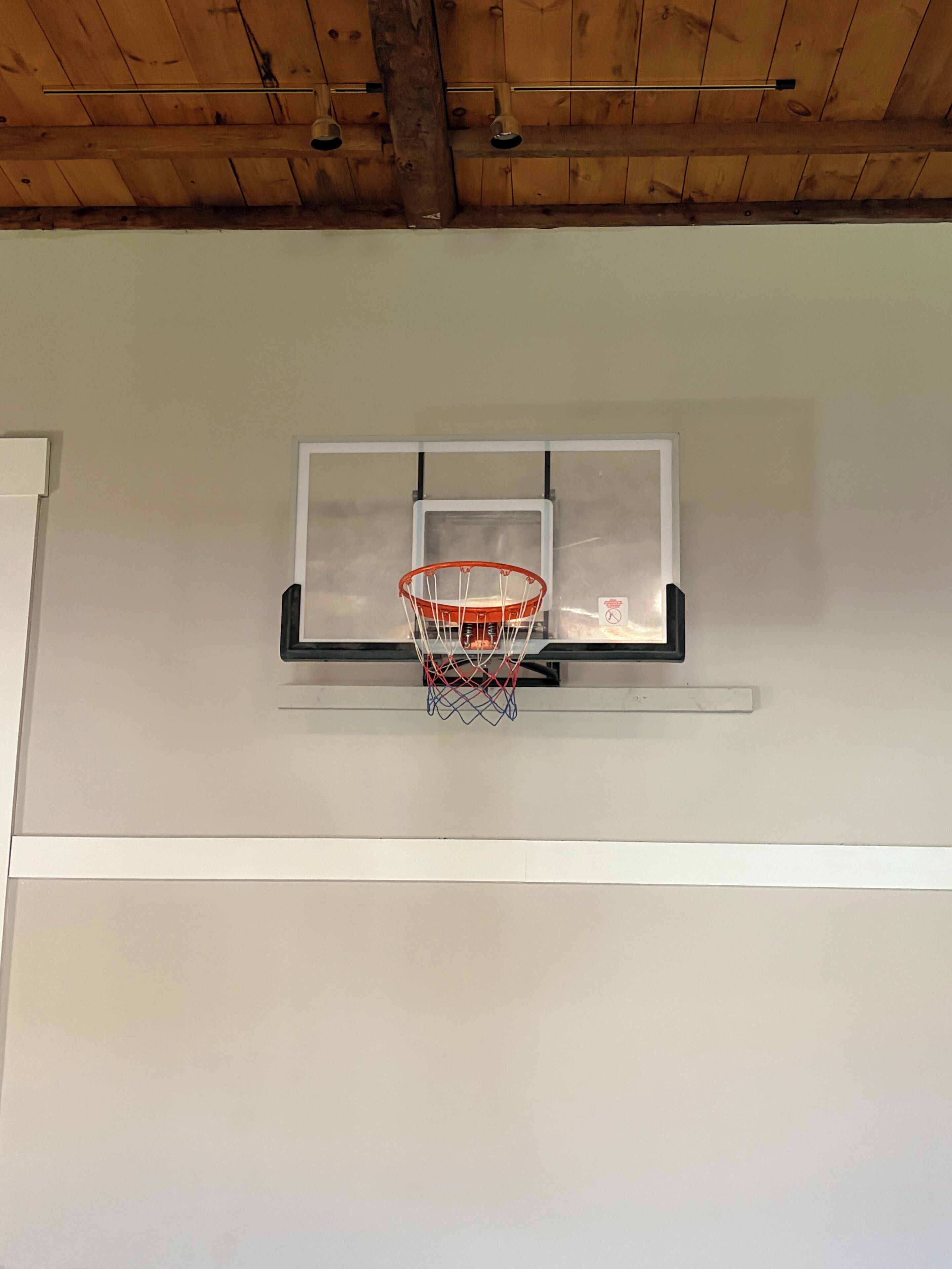 Un panier de basket fixé à un mur, avec un plafond en bois au-dessus.