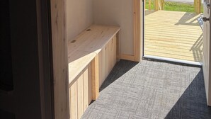 A room with a wooden bench, a small shelf, and a door leading to an outdoor area with a view of trees and a road. - Welcome to "the east Madison chapel" (Madison)