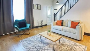 Una sala de estar con un sofá, un sillón, una mesa de centro, una escalera y una puerta.
