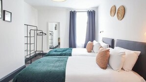 Habitación de hotel con dos camas, un armario, un perchero y una ventana con cortinas.