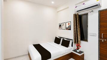 A bedroom with a bed, a nightstand, a window with curtains, and an air conditioning unit.