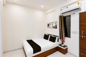 A bedroom with a bed, a nightstand, a window with curtains, and an air conditioning unit. - Classic Super Hotel O Khatu Shyam Temple (Danta Ramgarh)
