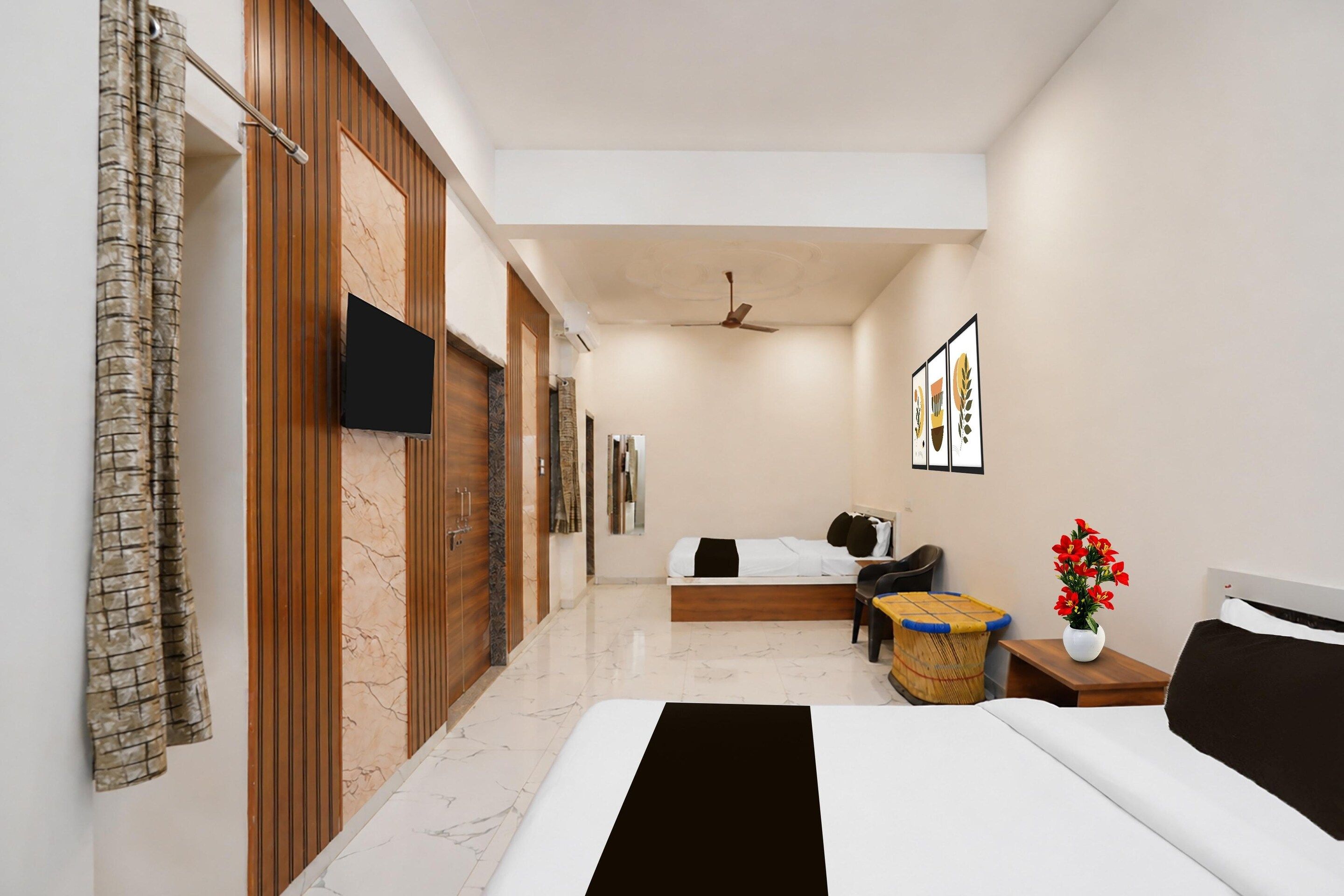 A hotel room with a bed, a flat-screen TV, a ceiling fan, a small seating area, and artwork on the walls.