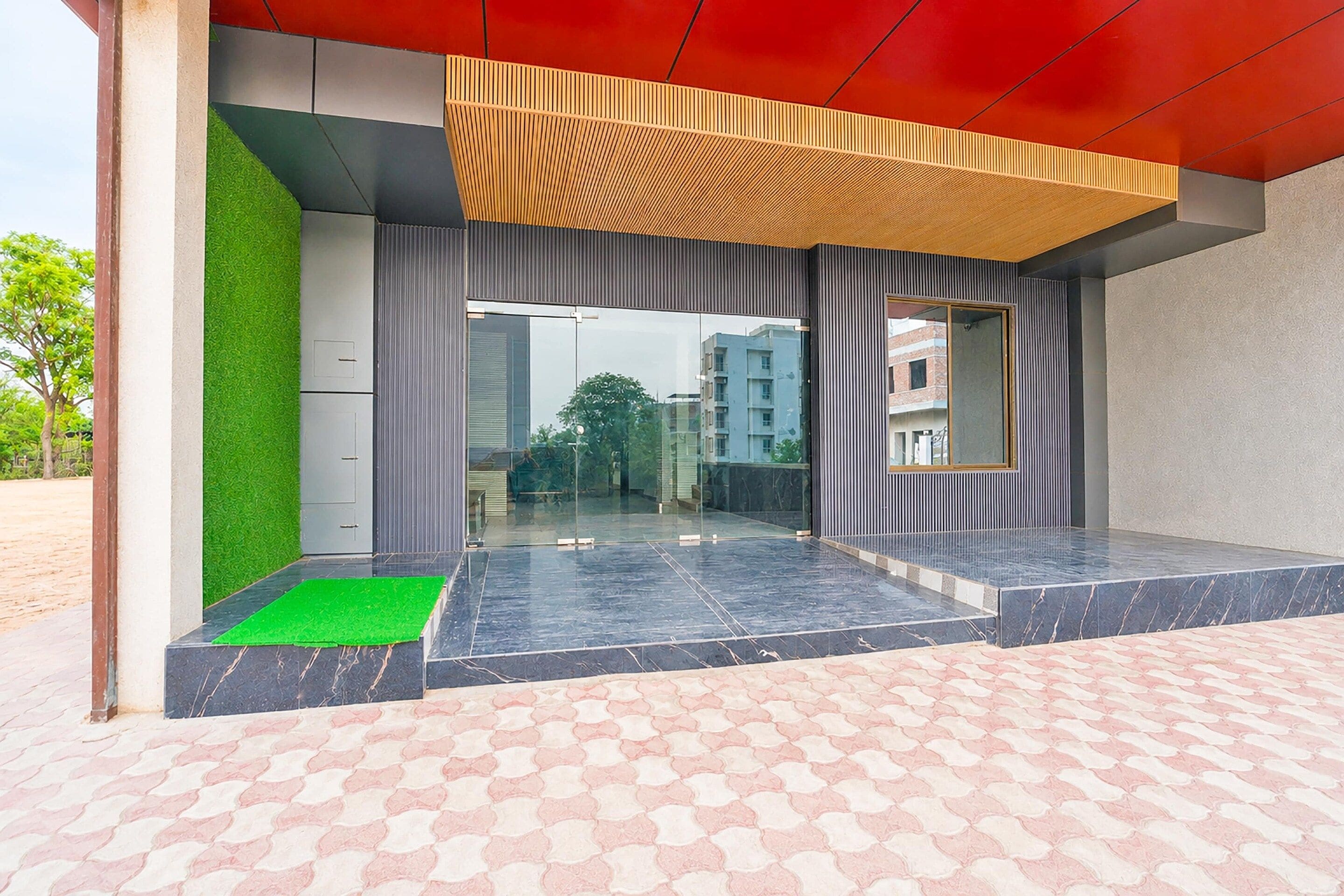 A modern building entrance with a glass door, a green mat, and a tiled floor.
