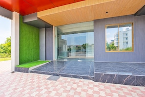 A modern building entrance with a glass door, green artificial grass, and a tiled floor. - Classic Super Hotel O Khatu Shyam Temple (Danta Ramgarh)